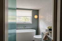 Robert Gordon Dish Wall Sconce in rose quartz ceramic mounted on bathroom wall above toilet near bathtub and window