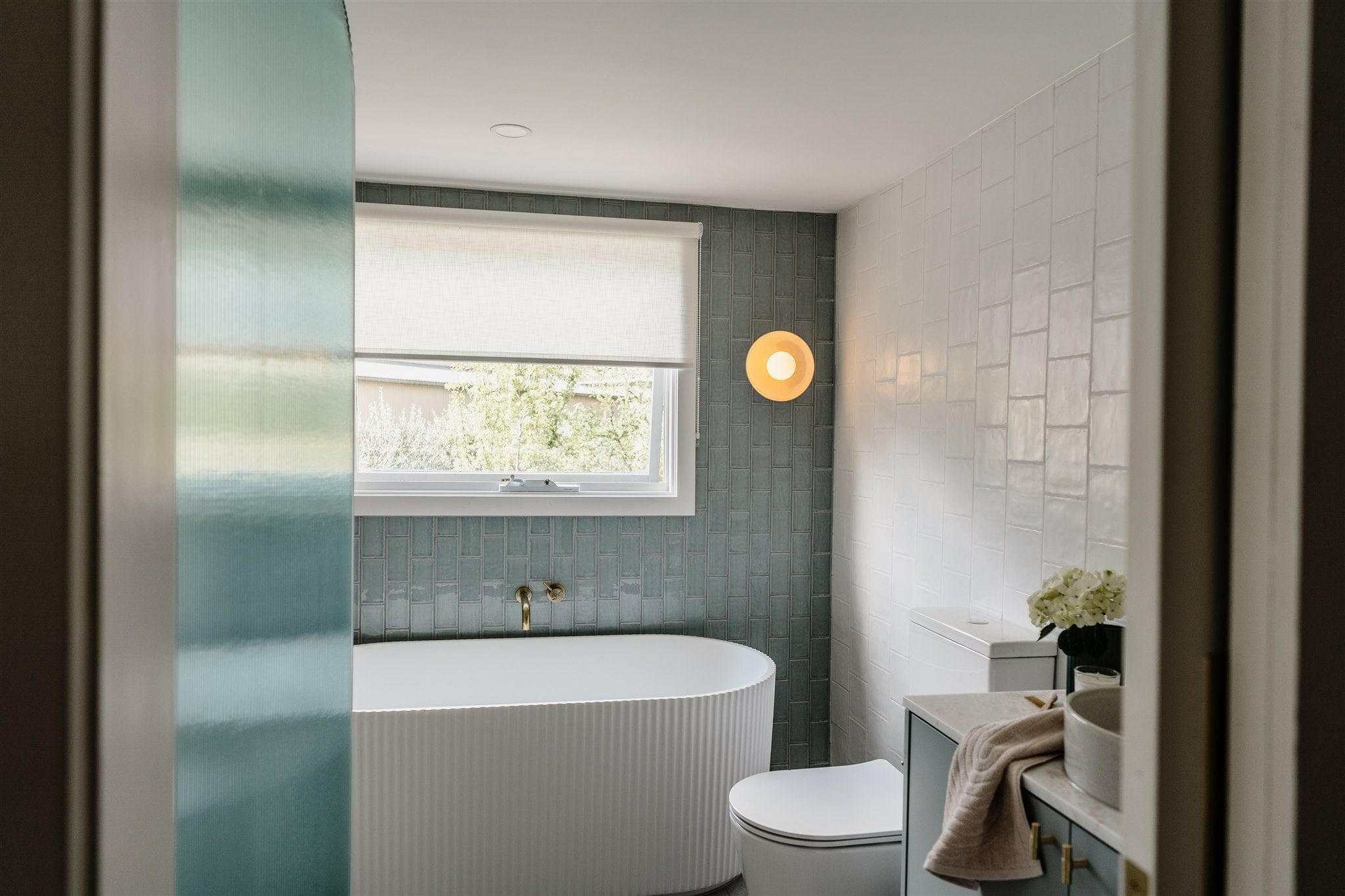 Robert Gordon Dish Wall Sconce in rose quartz ceramic mounted on bathroom wall above toilet near bathtub and window