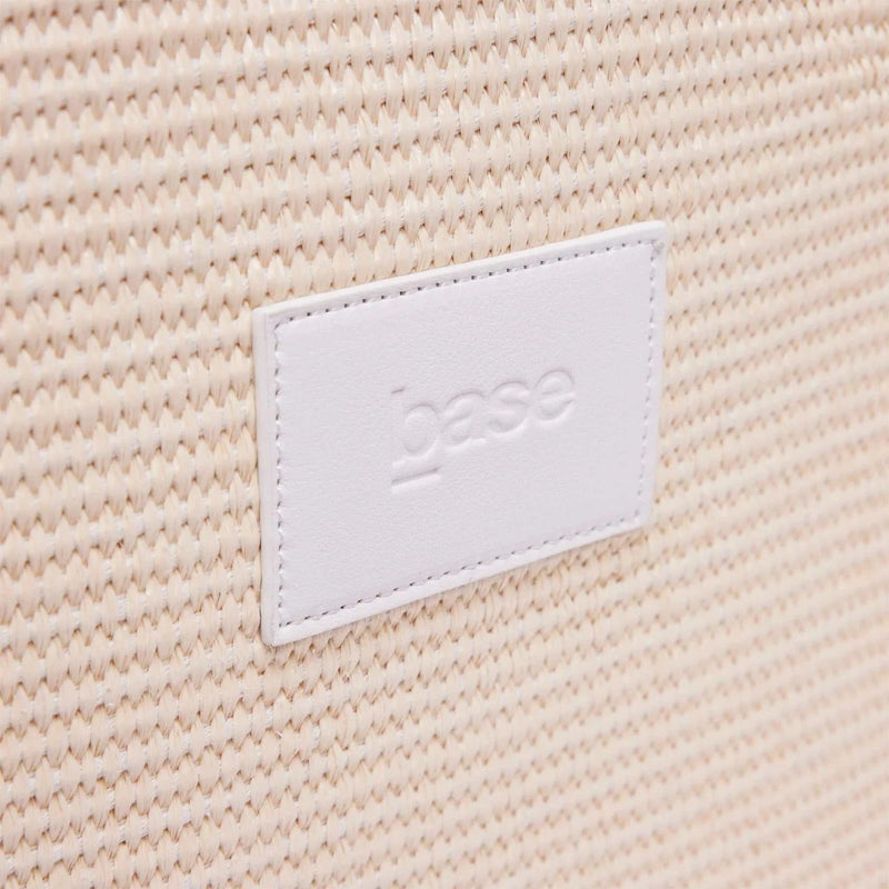 Close-up of woven polypropylene straw texture with white leather Base Supply Panier logo patch on chalk crossbody bag