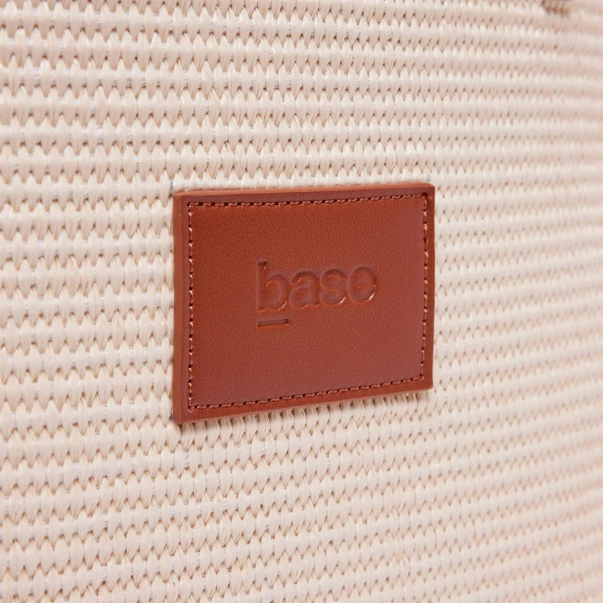 Close-up of woven tan polypropylene straw texture with brown leather Base Supply Panier label embossed on bag surface