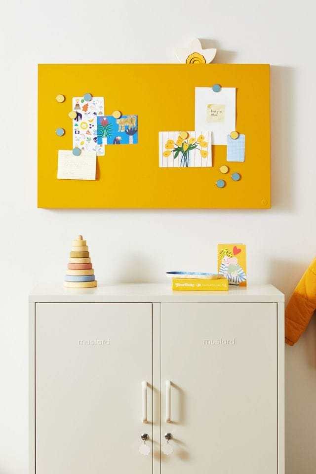 Mustard Made yellow magnetic buttons holding photos on board above white cabinet