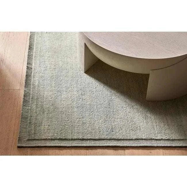 GlobeWest Bower Frame Rug in seafoam wool with hand-woven construction and layered border design on wooden floor