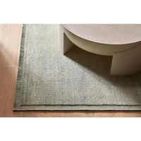 GlobeWest Bower Frame Rug in seafoam wool with hand-woven construction and layered border design on wooden floor