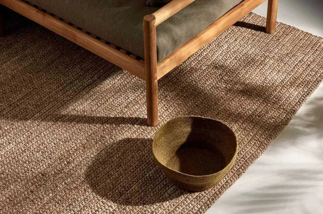 GlobeWest Harbour Knot outdoor rug in tawny color hand-woven from 100% PET yarn under wooden chair with woven basket on top