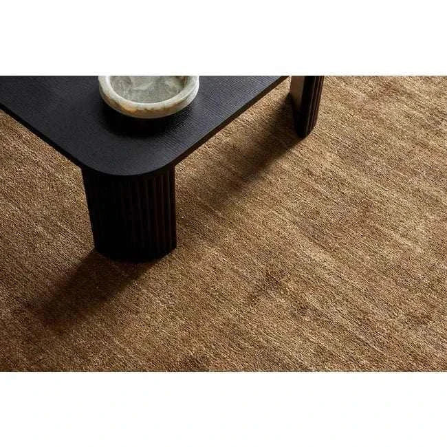Close-up of GlobeWest Tepih Dune Rug in olive wool blend with subtle pattern beneath black table leg.
