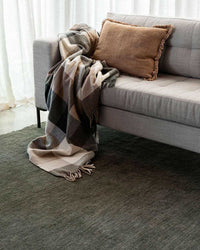 Forest green Sandringham Floor Rug with dense wool pile under a modern sofa with a brown fringed cushion and cozy plaid throw.