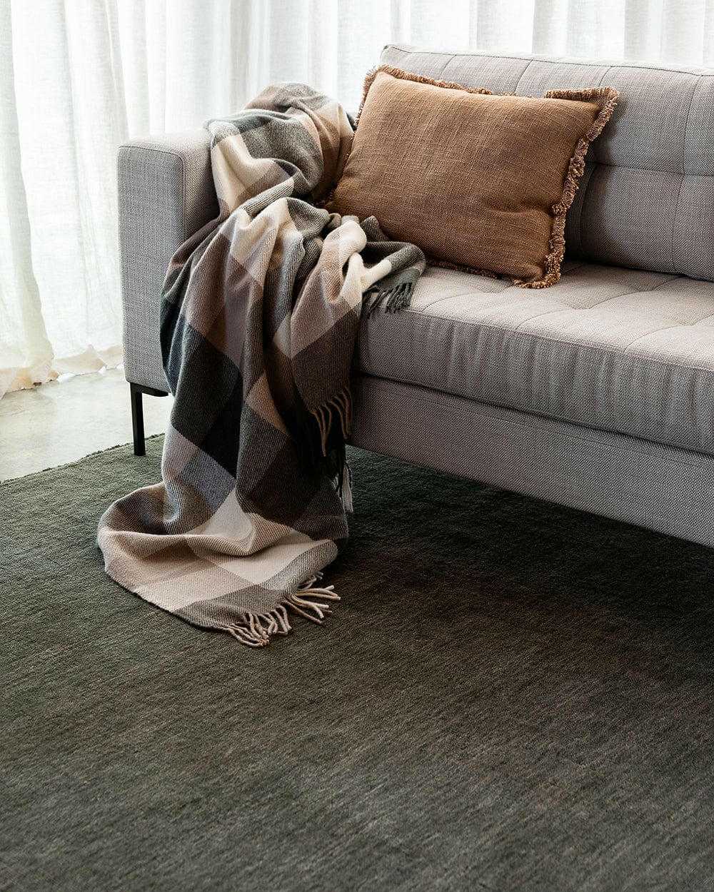 Forest green Sandringham Floor Rug with dense wool pile under a modern sofa with a brown fringed cushion and cozy plaid throw.