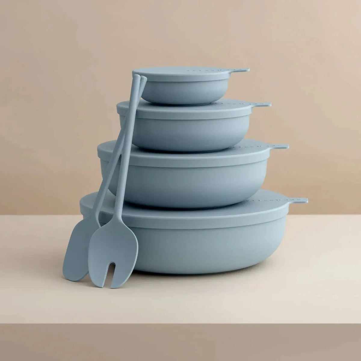 Set of four sky blue Styleware nesting bowls with lids and matching serving utensils, stackable and lightweight for versatile kitchen use.