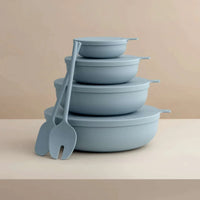 Set of four sky blue Styleware nesting bowls with lids and matching serving utensils, stackable and lightweight for versatile kitchen use.