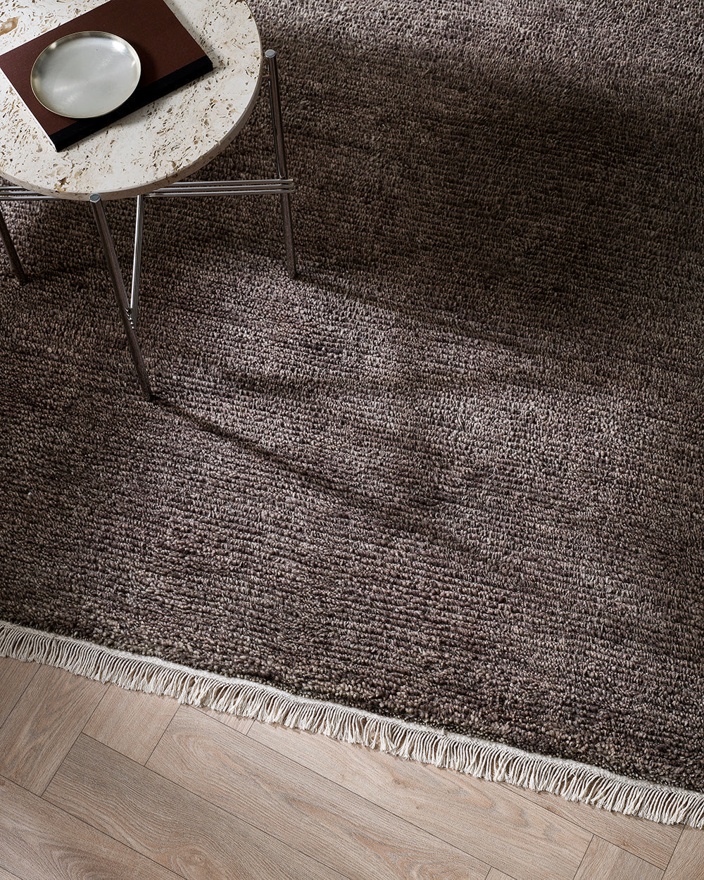 Baya Tanami Floor Rug in earthy brown with hand-knotted texture and soft cotton fringe on wooden floor under a round table