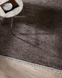 Baya Tanami Floor Rug in earthy brown with hand-knotted texture and soft cotton fringe on wooden floor under a round table