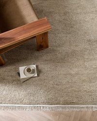 Baya Tanami Floor Rug in fossil taupe with hand-knotted texture and soft cotton fringe under wooden furniture
