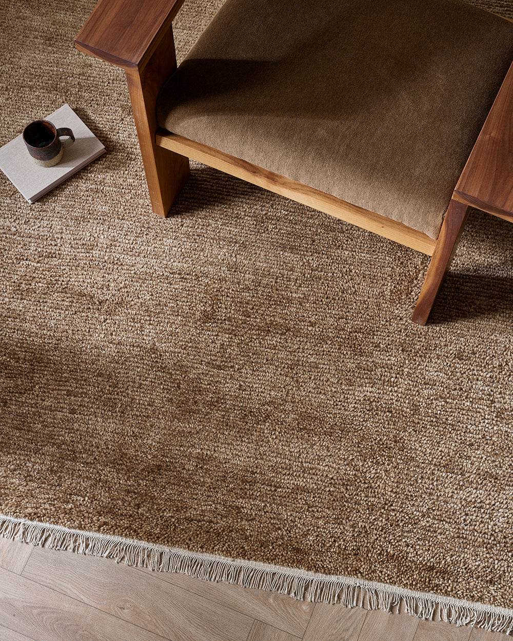 Baya Tanami Floor Rug in warm treacle tone with hand-knotted ribbed texture and soft cotton fringe under a wooden chair.