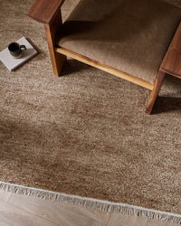 Baya Tanami Floor Rug in warm treacle tone with hand-knotted ribbed texture and soft cotton fringe under a wooden chair.