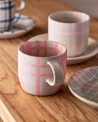 Robert Gordon Hand-Painted Mug with pink tartan checks, ceramic stoneware, 350ml capacity on wooden table with matching plates and another mug in background