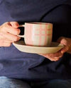 Robert Gordon Hand-Painted Mug with pink and cream tartan pattern held on a beige saucer