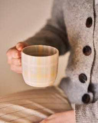 Robert Gordon hand-painted ceramic mug with tartan check design held by person in grey buttoned sweater