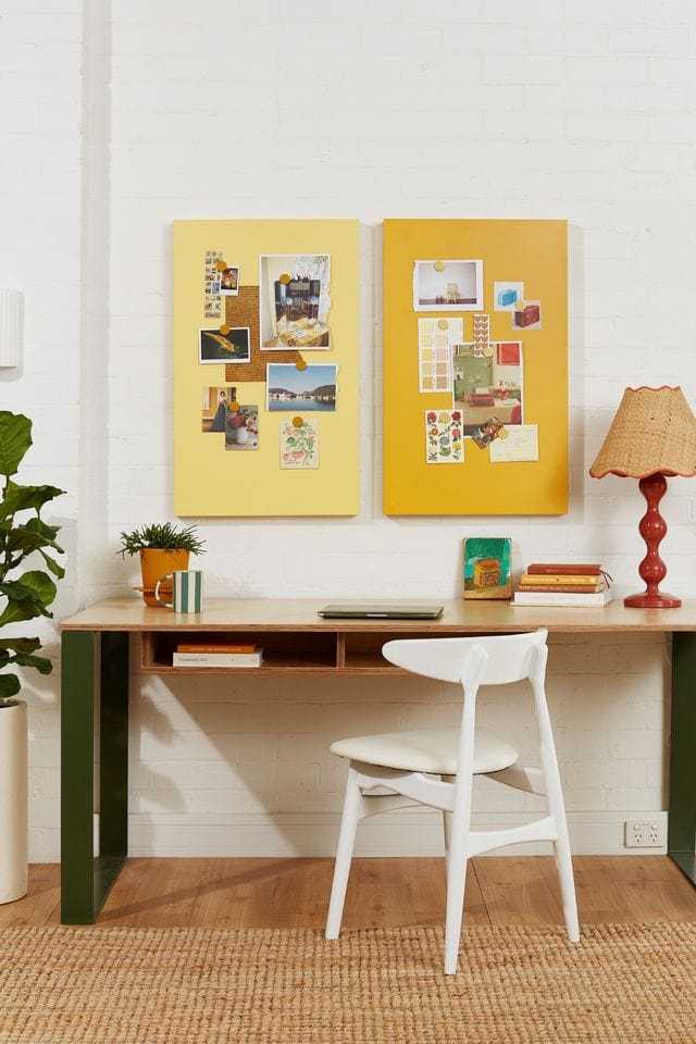 Two mustard yellow magnetic storyboards mounted on a white brick wall above a wooden desk with a white chair, next to a red lamp and green plant, perfect for organizing plans and matching Mustard Made lockers.
