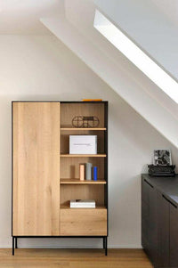 Ethnicraft Blackbird Storage Cupboard in natural oak with one door, drawer, and open shelves in a modern room setting