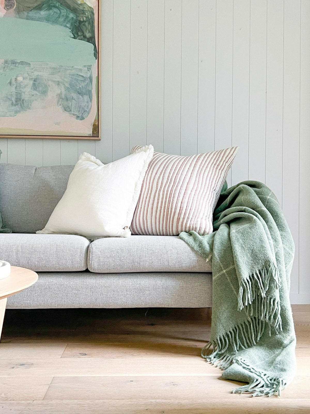 Eadie Lifestyle Luca Boho white linen cushion with hand-frayed edges on grey sofa with green throw blanket