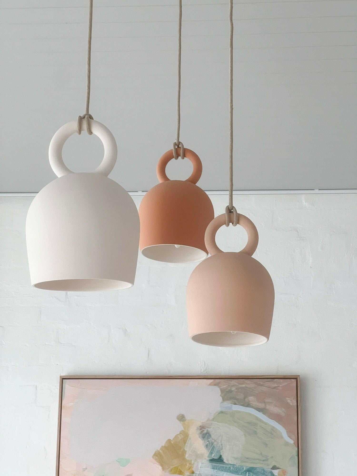 POTT Lighting Calo Pendant in salmon and neutral tones, handmade bell-shaped ceramic lights with natural jute rope suspension.