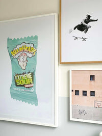 Dom Gauci Kids Art Print Sour Power featuring Warheads Extreme Sour candy packaging illustration in a white frame displayed on a wall.