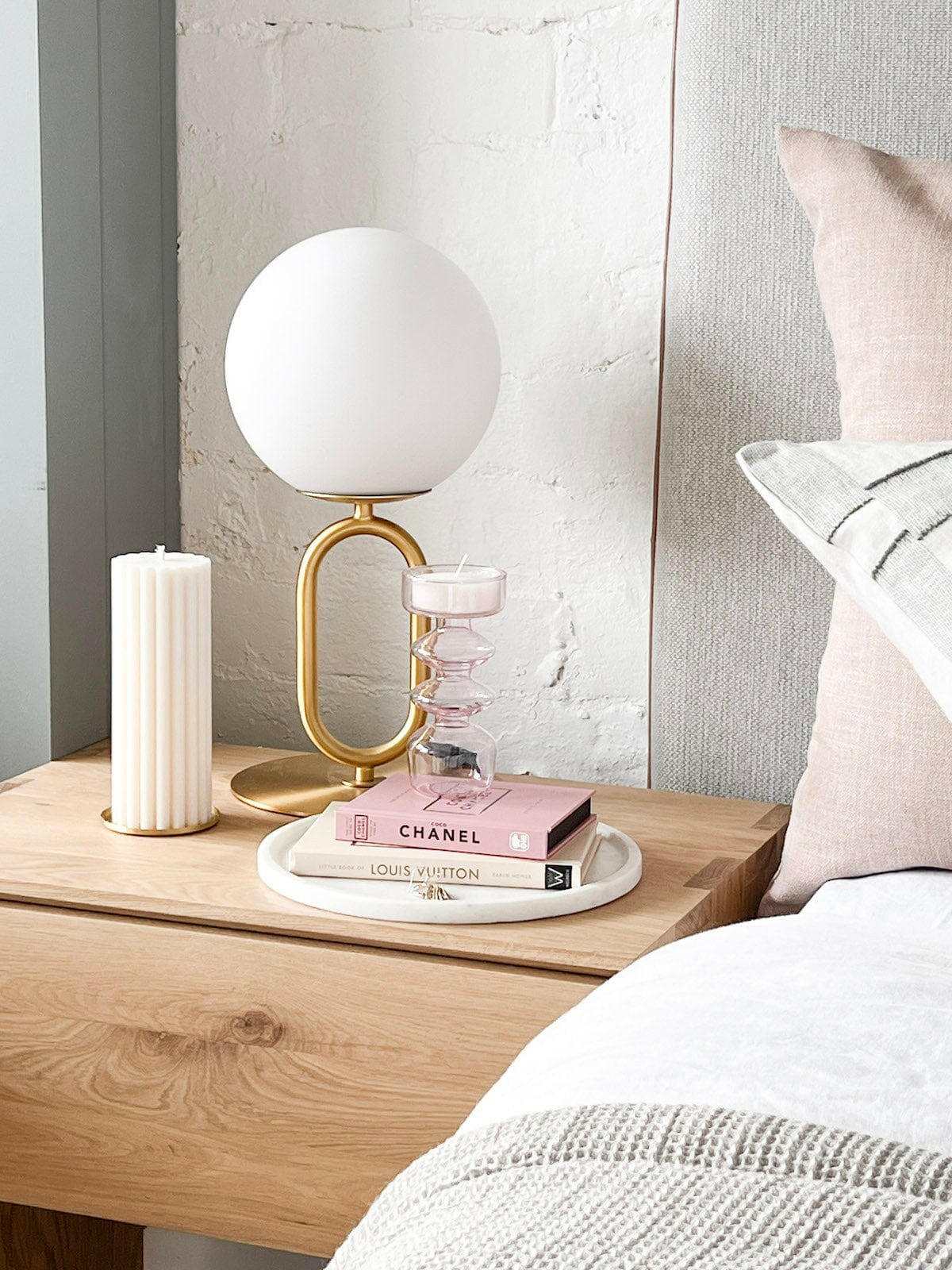 Modern brass desk lamp with frosted glass shade on wooden bedside table with books and candle
