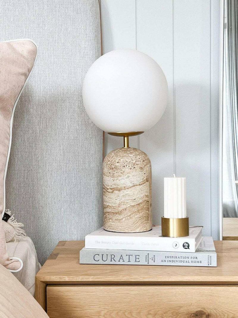 Soren Desk Lamp with travertine base, frosted glass globe shade, and brass details on wooden bedside table