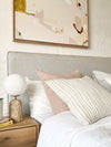 norsu Studio Washable Cushion in blush on bed with textured white cushion and bedside decor