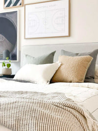 norsu Studio Bouclé Buff cushion with white leather piping on a bed with neutral bedding and gray pillows