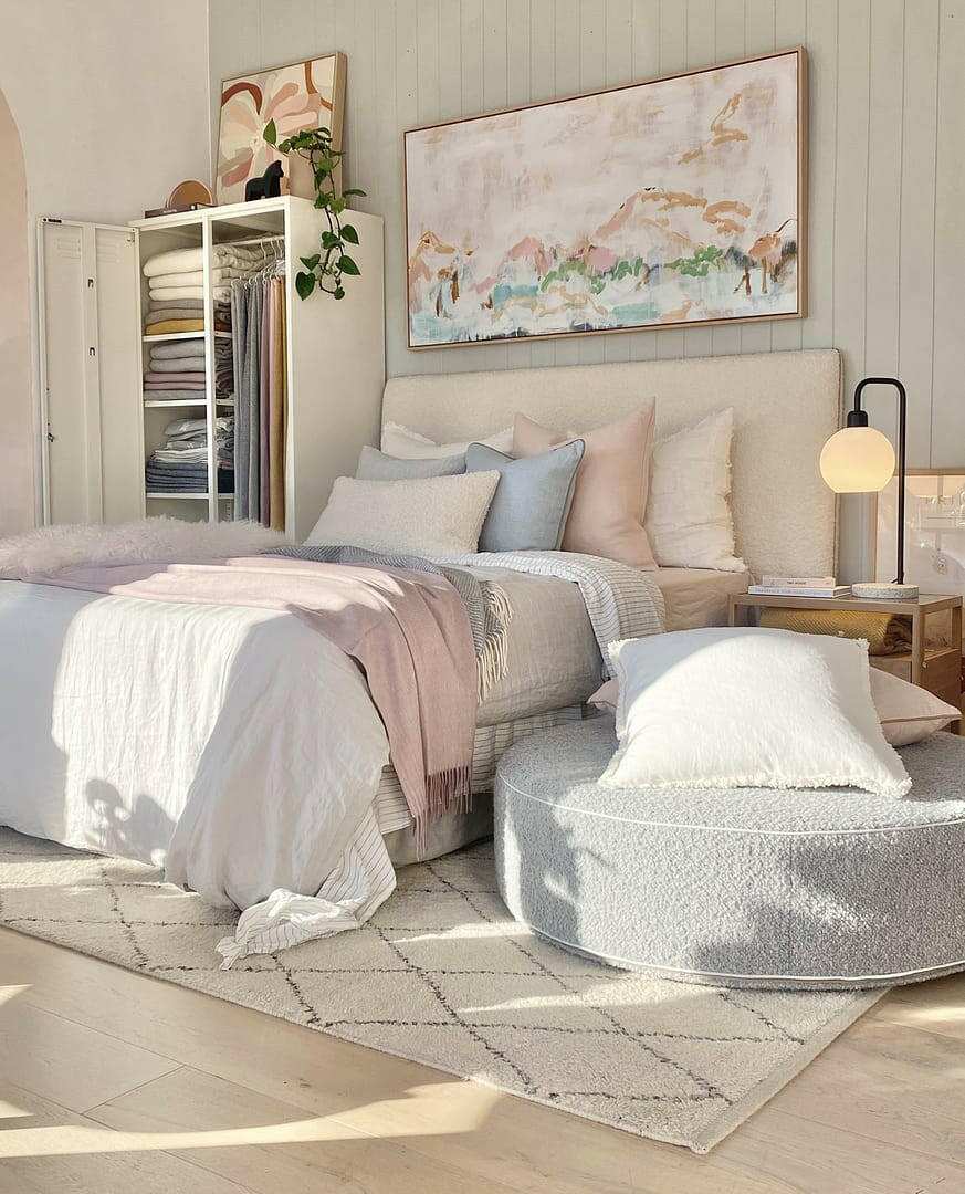 Soft, round norsu Design your Own Ottoman in light boucle fabric placed in a cozy modern bedroom setting with neutral bedding and minimal decor.