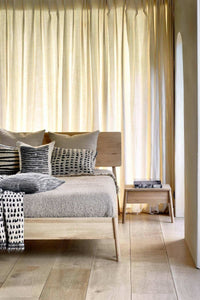 Ethnicraft Oak Air Bedside Table with 1 drawer in natural oak beside a wooden bed in a bright bedroom