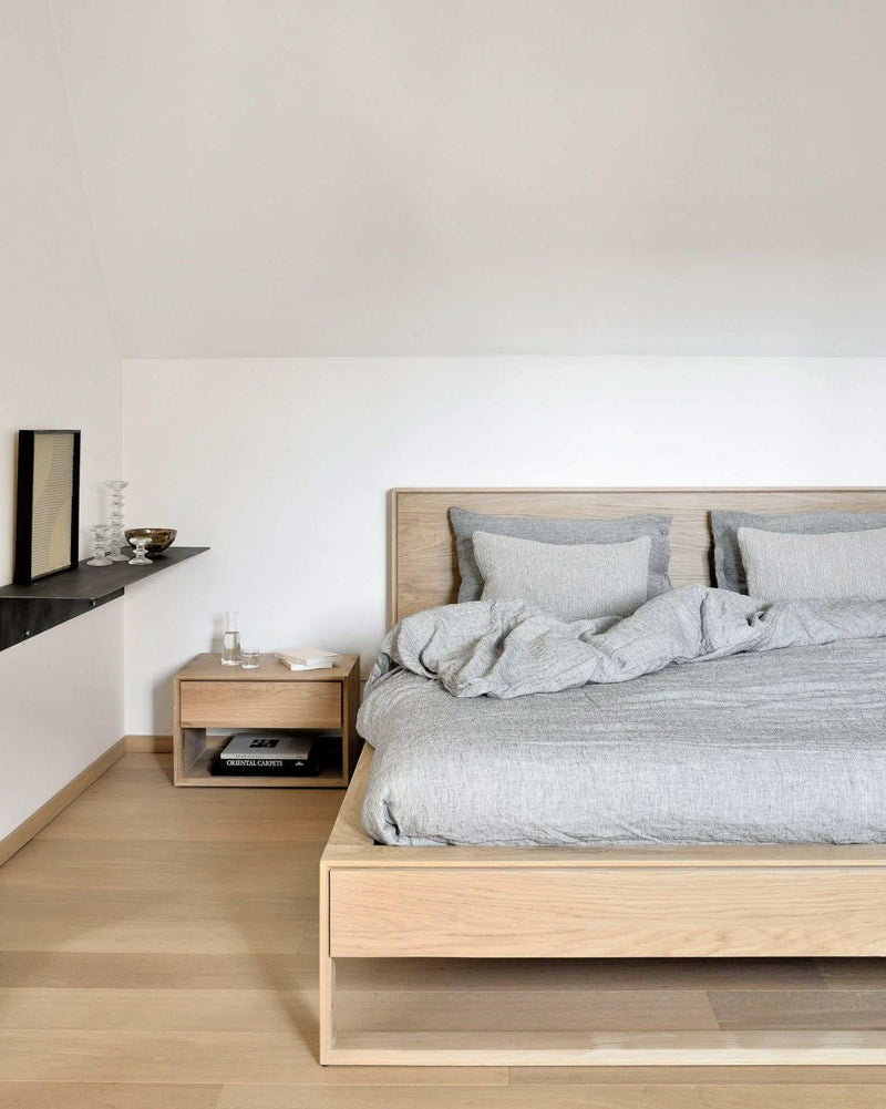 Ethnicraft Nordic II Bedside Table in natural oak with one drawer next to a modern wooden bed in minimalist bedroom
