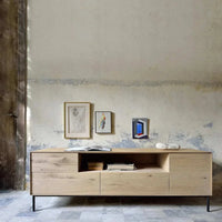 Ethnicraft Whitebird Entertainment Unit in natural oak with 1 door, 1 flip-down door, and 2 drawers, featuring solid European oak and slim black legs.