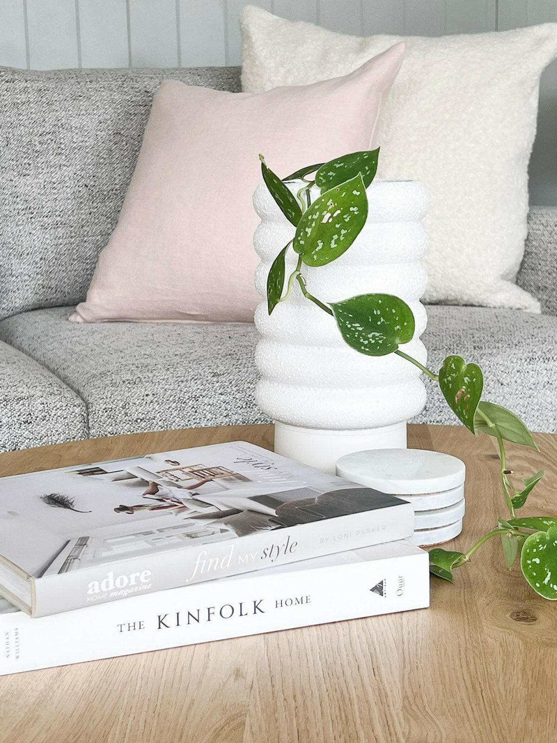 White textured bubbly Alder Pot planter with green trailing plant on wooden table with books and cushions in background