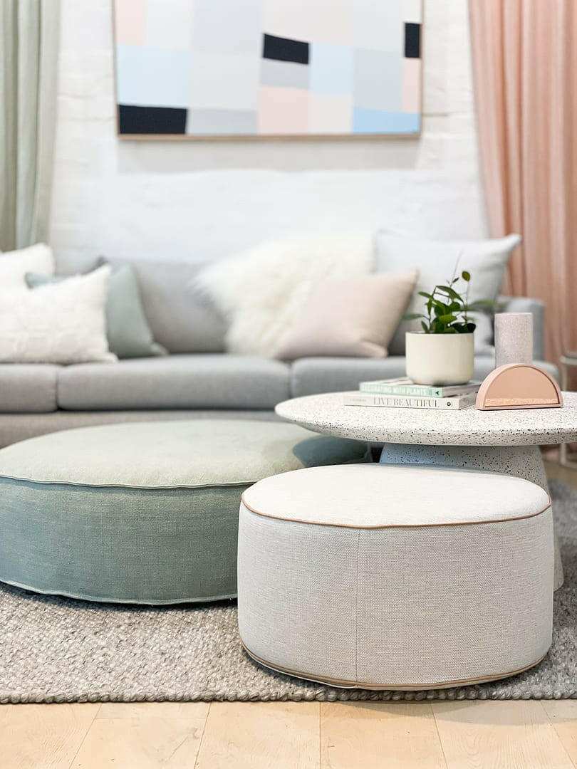 Round soft fabric ottomans in blush and sage colors in modern living room with grey sofa and abstract wall art