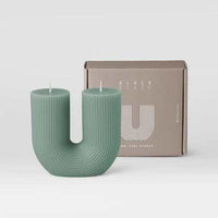 Modern green U-shaped Black Blaze candles with ribbed texture beside branded packaging box