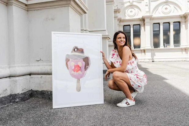 Woman in floral dress crouching beside a framed DG Designs Dom Gauci kids art print of a melting 90's ice cream treat outdoors