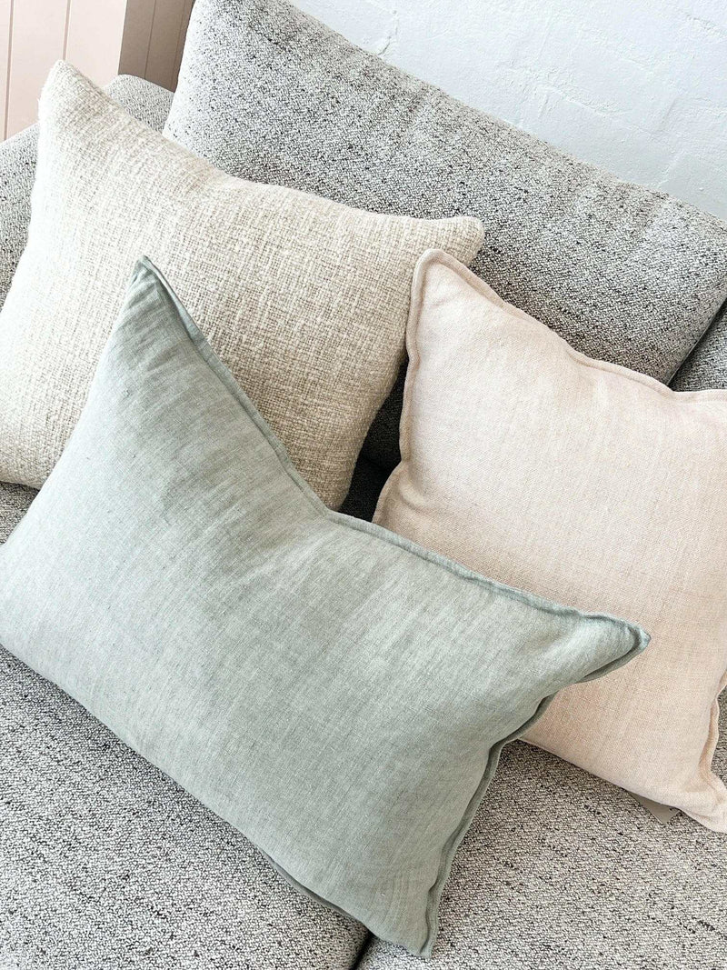 Baya Arcadia Cushion in sage green linen with flange edge on a grey textured sofa