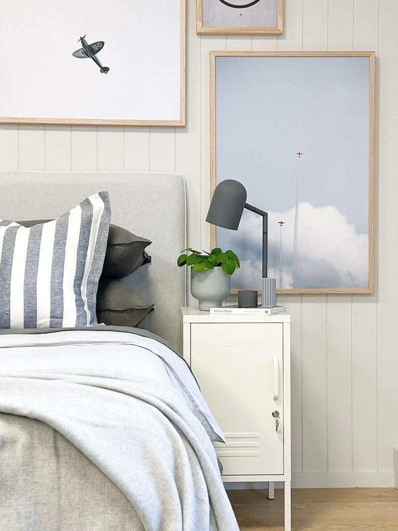 Modern charcoal Pia desk lamp on white bedside table next to bed with gray and white striped pillow and framed artwork on wall