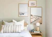 Bedroom interior with wing print wall art in various sizes, framed and hanging above a bed with neutral pillows and a bedside table with a lamp and books.
