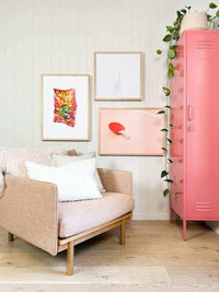 Pink Mustard Made Locker standing next to a beige armchair in a stylish living room with framed wall art and a plant.