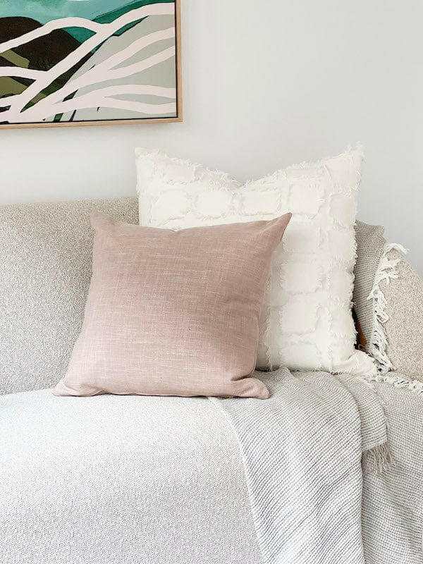 Blush norsu Studio Washable Cushion on a sofa with a white textured cushion and a light gray throw blanket
