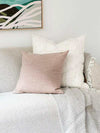 Blush norsu Studio Washable Cushion on a sofa with a white textured cushion and a light gray throw blanket