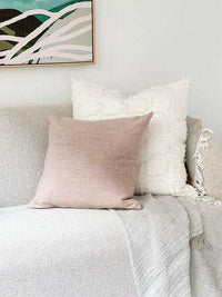 Blush norsu Studio Washable Cushion on a sofa with a white textured cushion and a light gray throw blanket