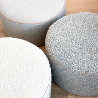 Three round norsu Design your Own Ottomans in different textured fabrics with blush leather piping on a wooden floor.