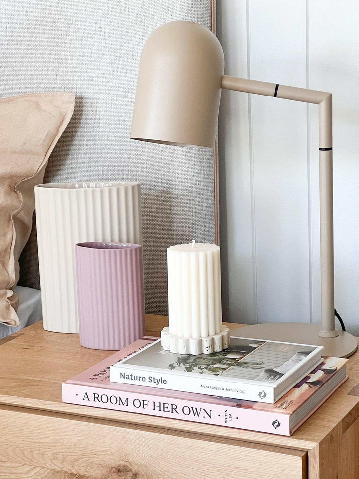 Modern bone-colored Pia Task Lamp with adjustable arm on wooden desk beside books and decorative candles
