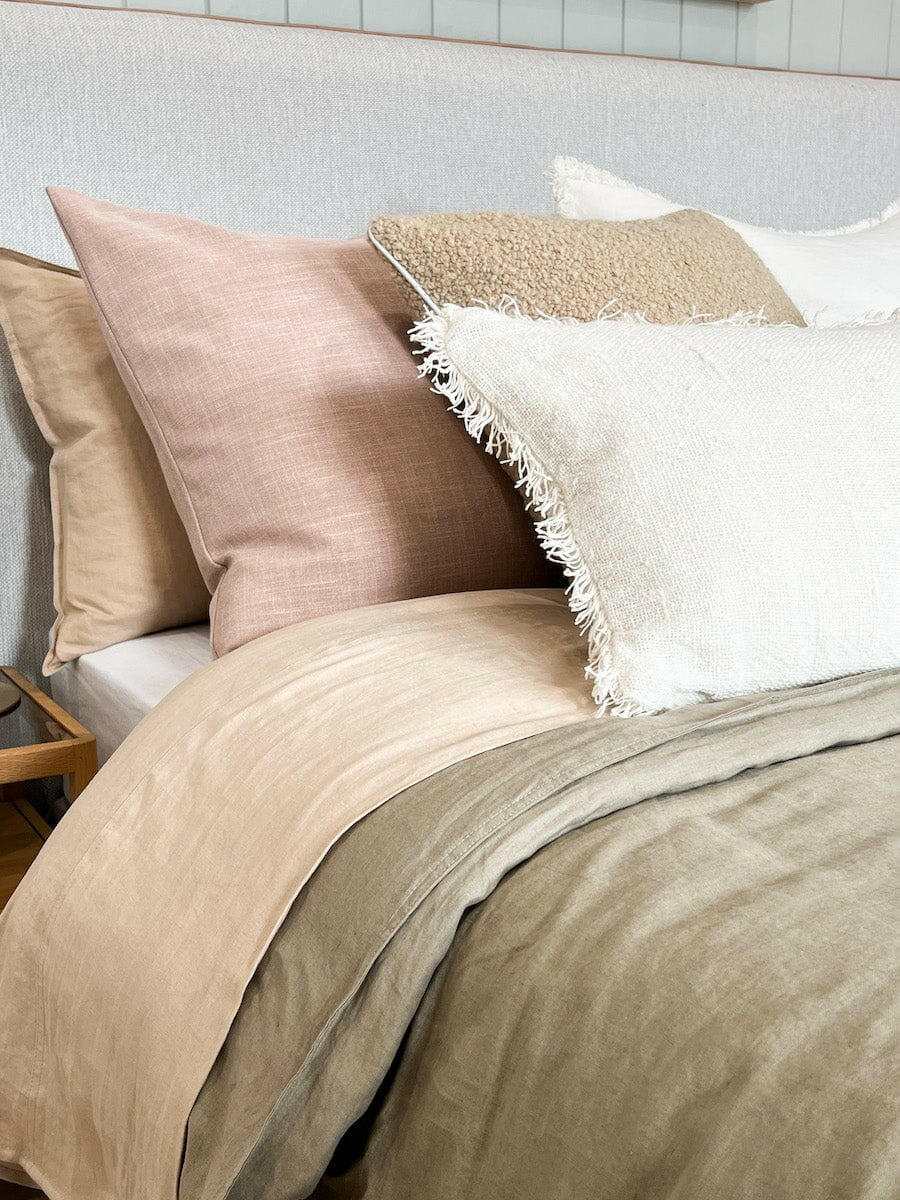 norsu Studio Washable Cushion in blush on a bed with neutral-toned pillows and blankets