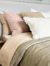 norsu Studio Washable Cushion in blush on a bed with neutral-toned pillows and blankets