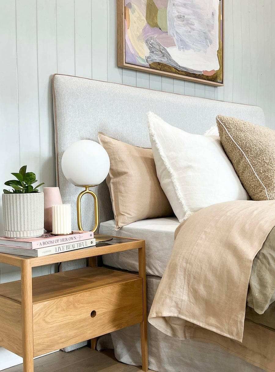 Ethnicraft Spindle Bedside table in natural oak with single drawer and smokey glass top next to bed with beige and white pillows